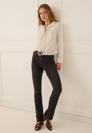A woman modeling a white long-sleeve lace blouse tucked into dark charcoal jeans with a brown belt and brown sandals