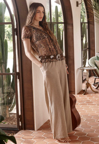 A woman stands barefoot in a rustic indoor setting with arched windows and terracotta tile flooring