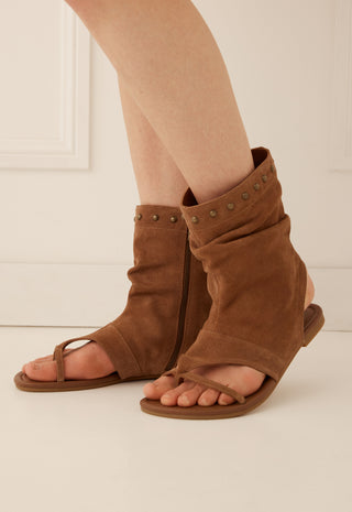 A pair of brown suede slide sandals with wraparound ankle straps and metal studs